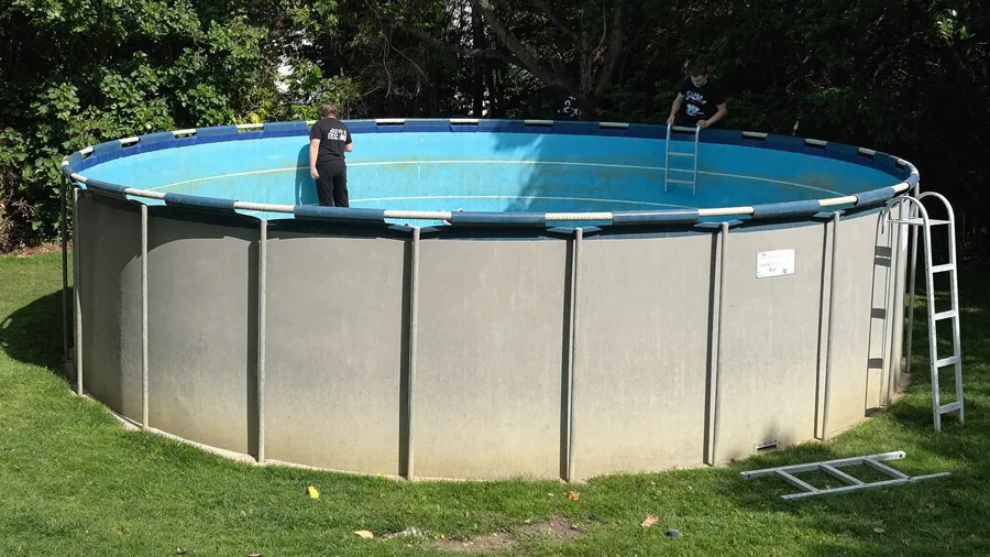 Workers taking apart an old above-ground pool wall in a backyard